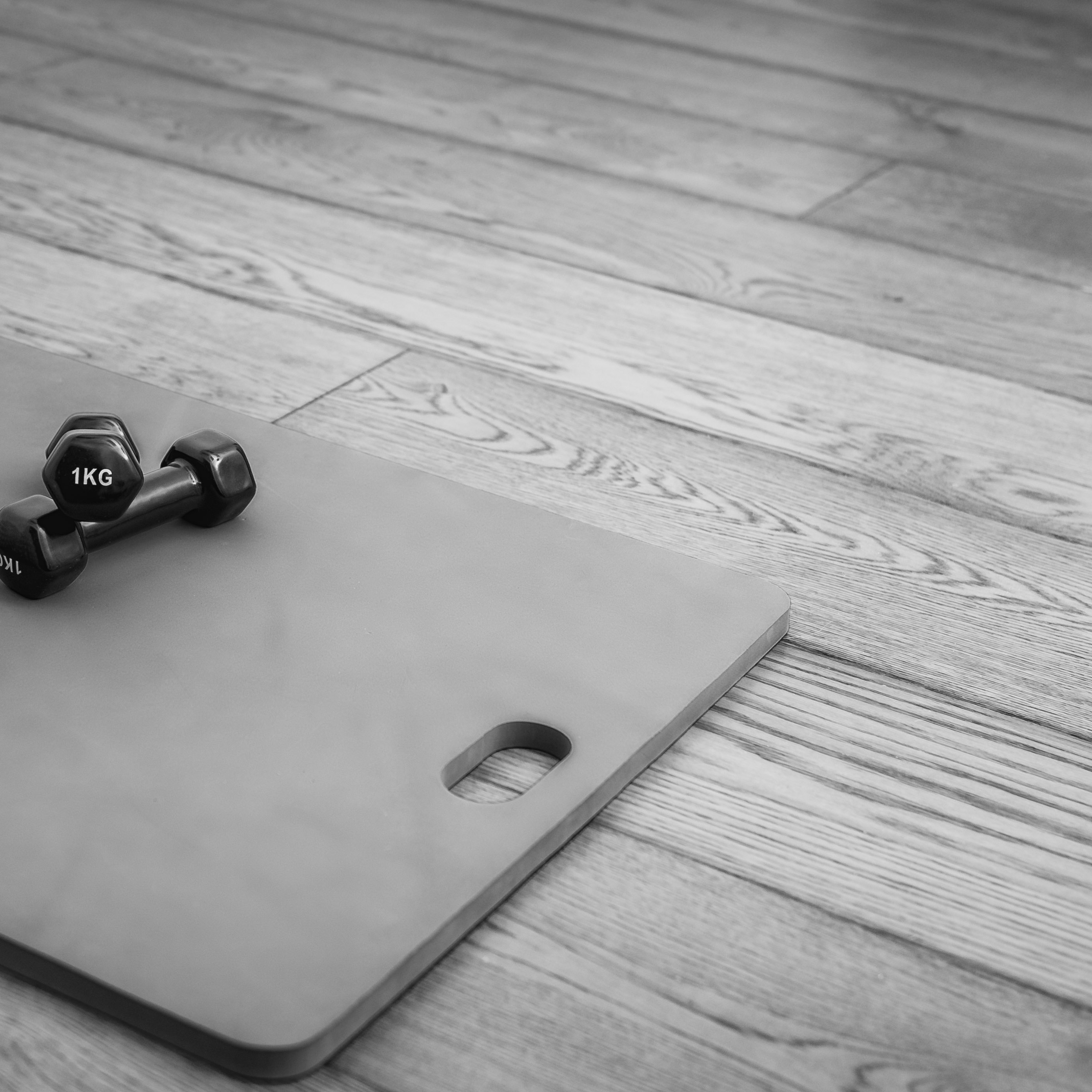 black and white photo showing a pilates mat with a set of weights in a studio
