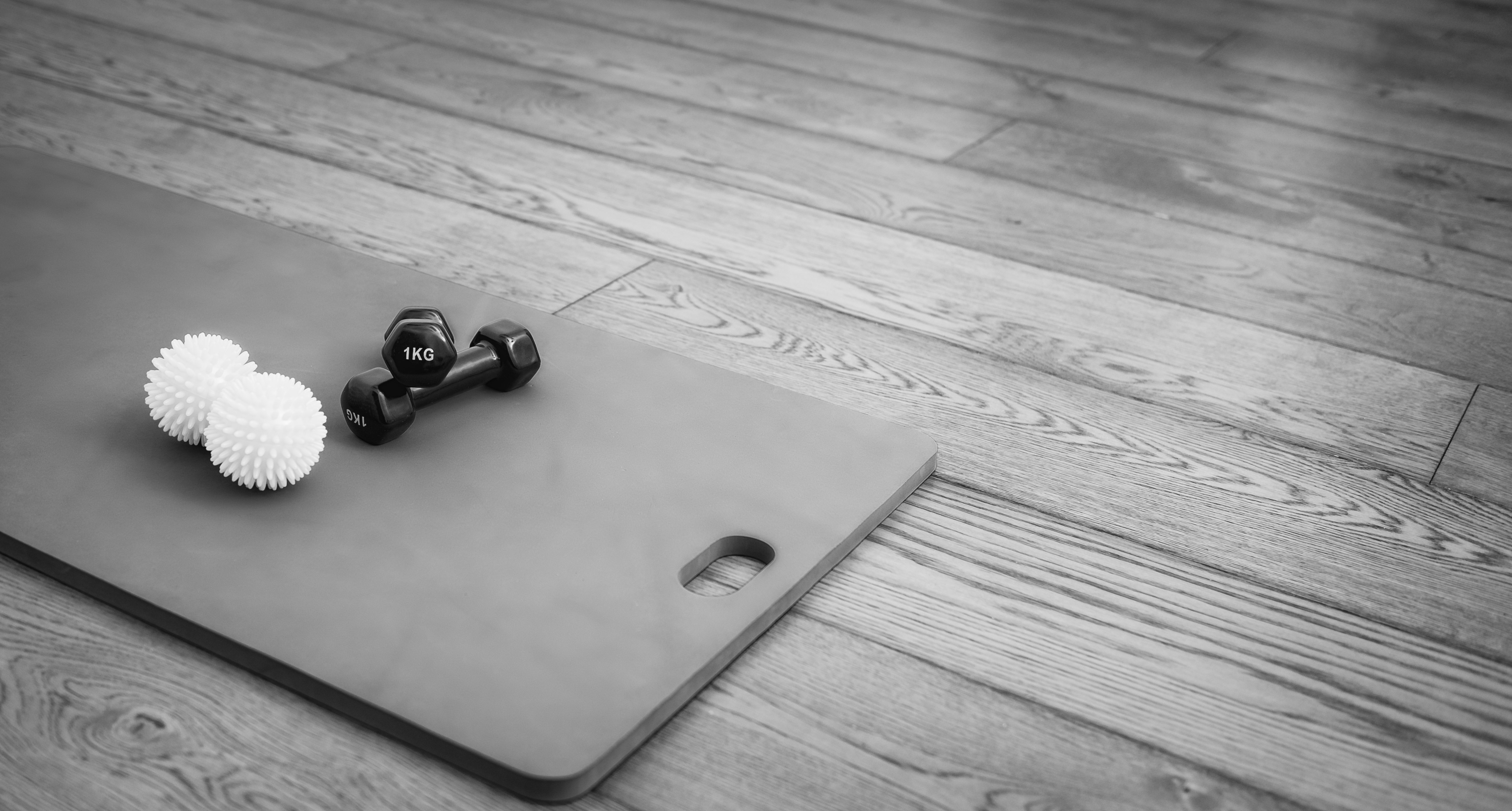 black and white photo showing a pilates mat with a set of weights in a studio